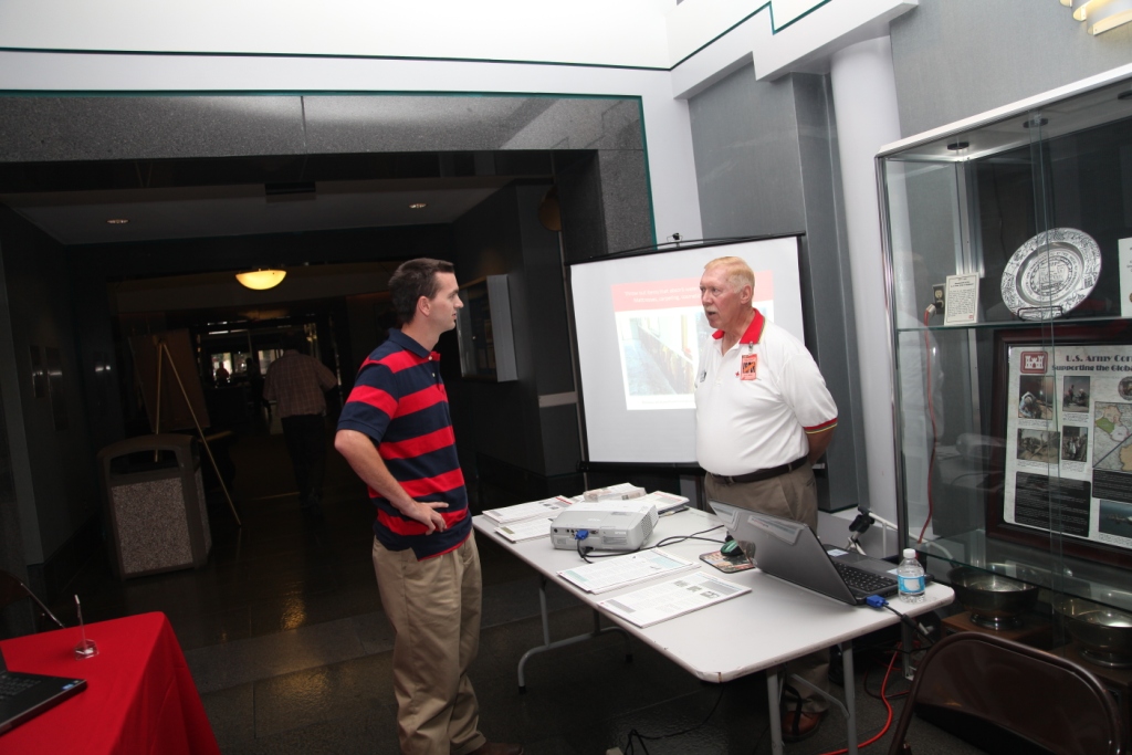 Attendees at an emergency preparedness fair standing at informational booths and tables with brochures and displays about hurricane preparedness, emergency supply kits and evacuation planning.