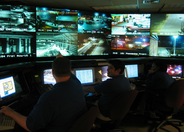 Security operations center interior with multiple monitors displaying security dashboards and analysts working at consoles.
