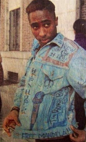 Color photograph of Tupac Shakur in 1988 wearing a denim jacket, portrait-style image.