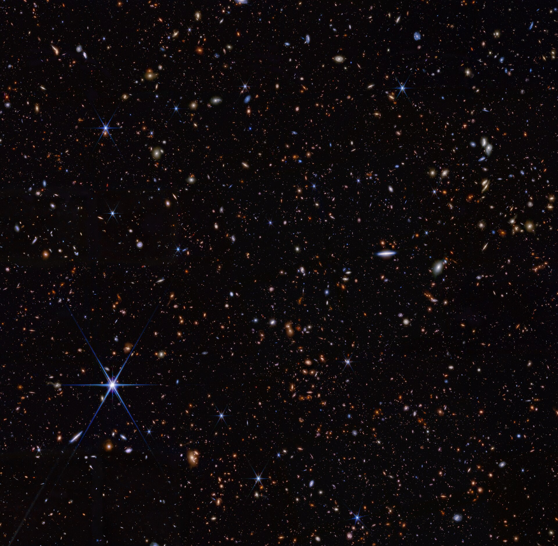James Webb Space Telescope NIRCam image from the JADES program showing a field of thousands of faint distant galaxies with a small, highlighted, very-high-redshift galaxy (JADES‑GS‑z14‑0) appearing as a tiny early‑universe dot.