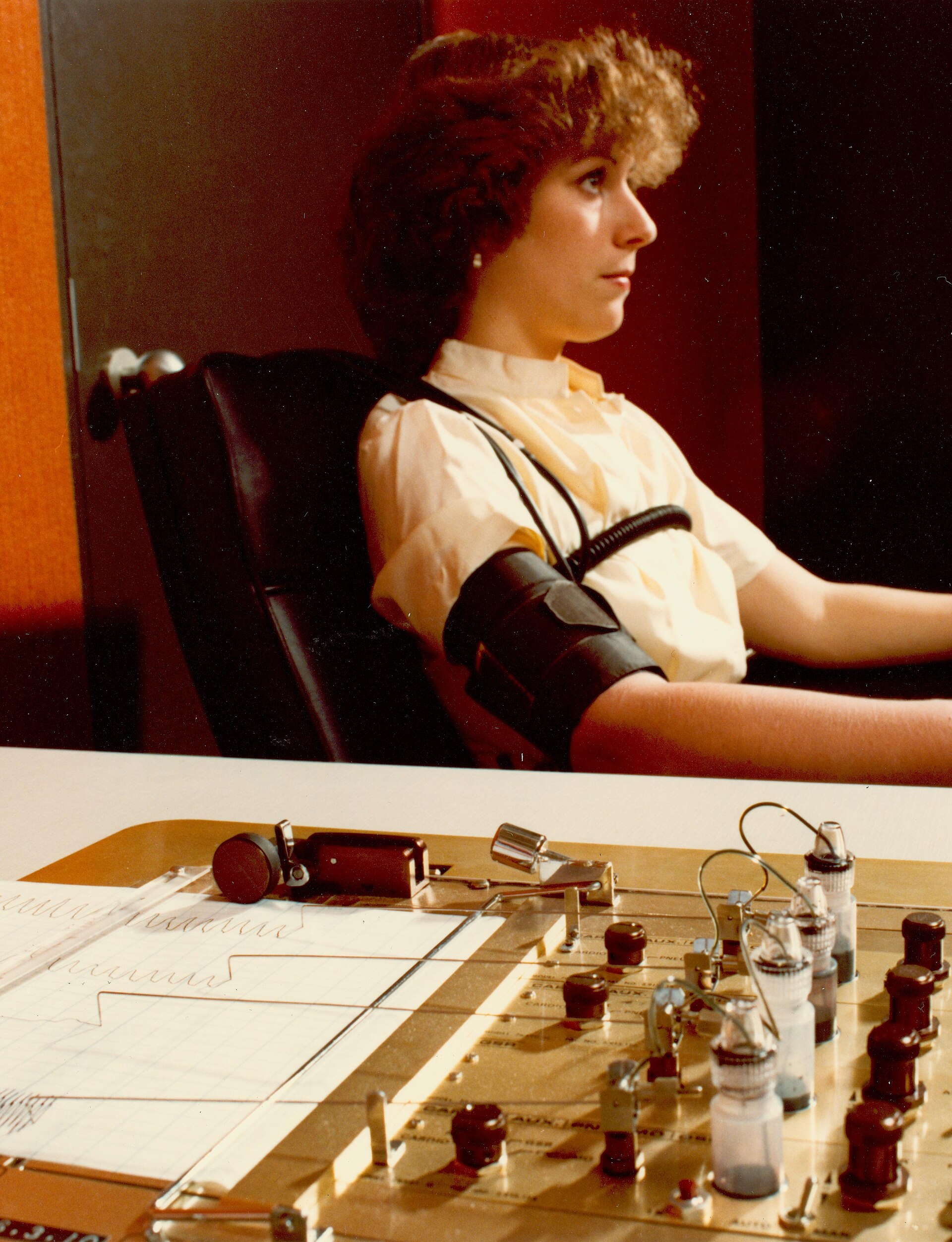 Technician administering a polygraph exam, with the polygraph machine readouts visible and the examiner making notes.